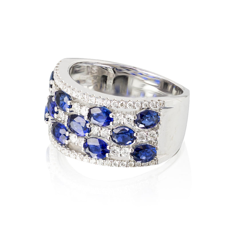 18kt white gold oval blue sapphire and diamond band. Ring consists of 11 oval blue sapphires set horizontally in 3 rows weighing 2.58cttw, and diamonds weighing 0.52cttw. Finger size 6.5